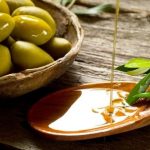olivový olej na dřevěné lžičce, listy olivovníka a čerstvé olivy v misce