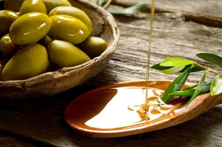 olivový olej na dřevěné lžičce, listy olivovníka a čerstvé olivy v misce