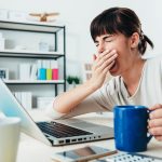 žena zíva při počítaci, v ruce drží šálku kávy
